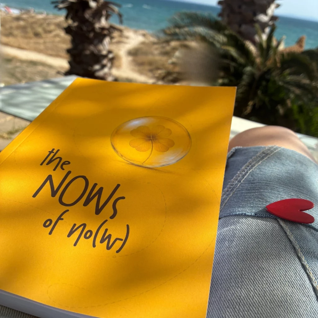The Nows of No(w) book by Pa3, on the lap of a reader on the beach
